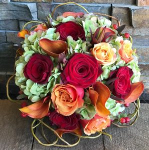 A vibrant bouquet of mixed flowers, including red and orange roses,  tied together for home decor with flowers